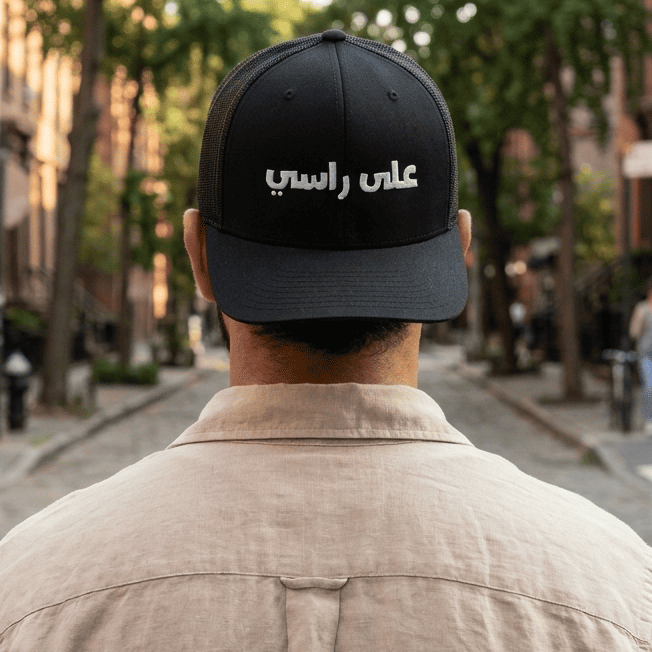 Model wearing 3ala Rasi embroidered trucker cap, Arabic slogan headwear by BOSA